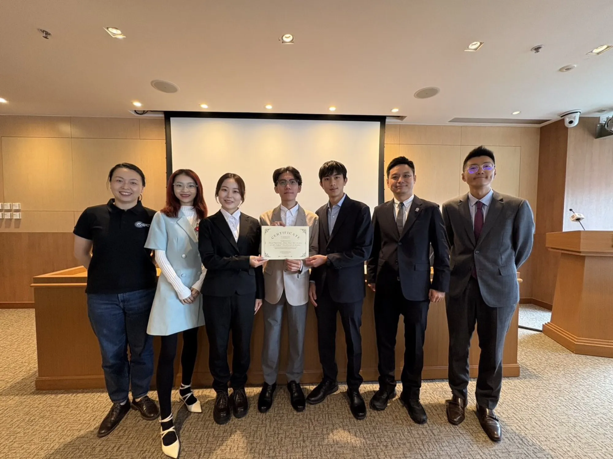 Seven people standing in a lecture room at ACTION 2025; two in the centre hold a certificate.