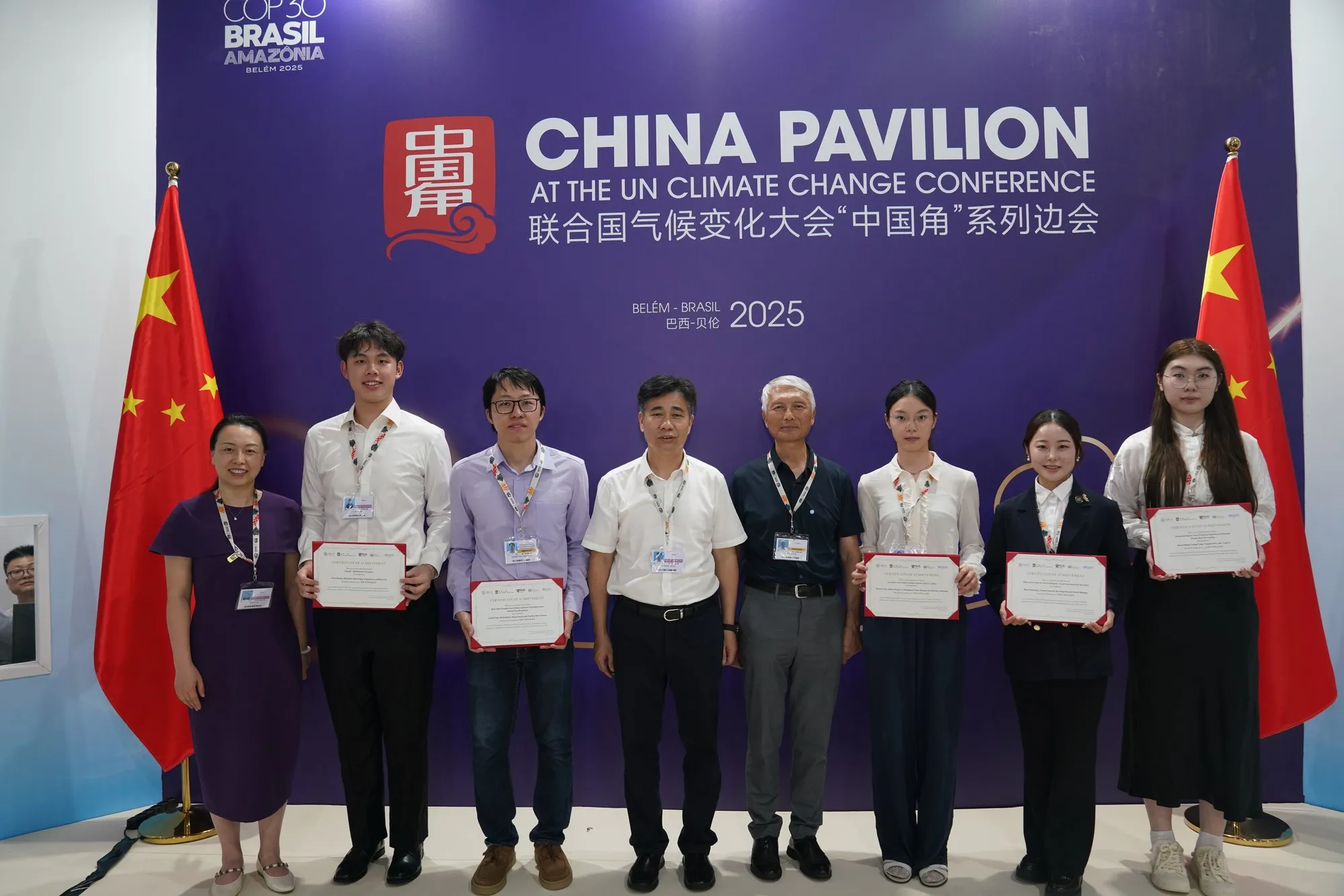 Eight people stand in front of the China Pavilion backdrop at COP30 in Belém; five of them hold certificates.