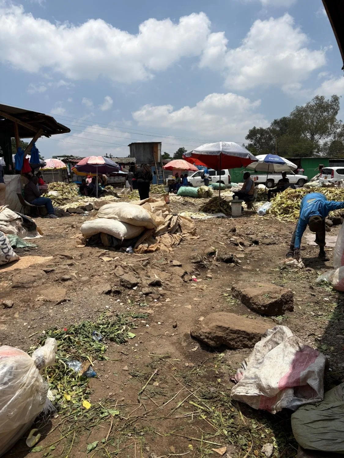 An open-air market: sacks, heaps of maize husks and traders under sun umbrellas.