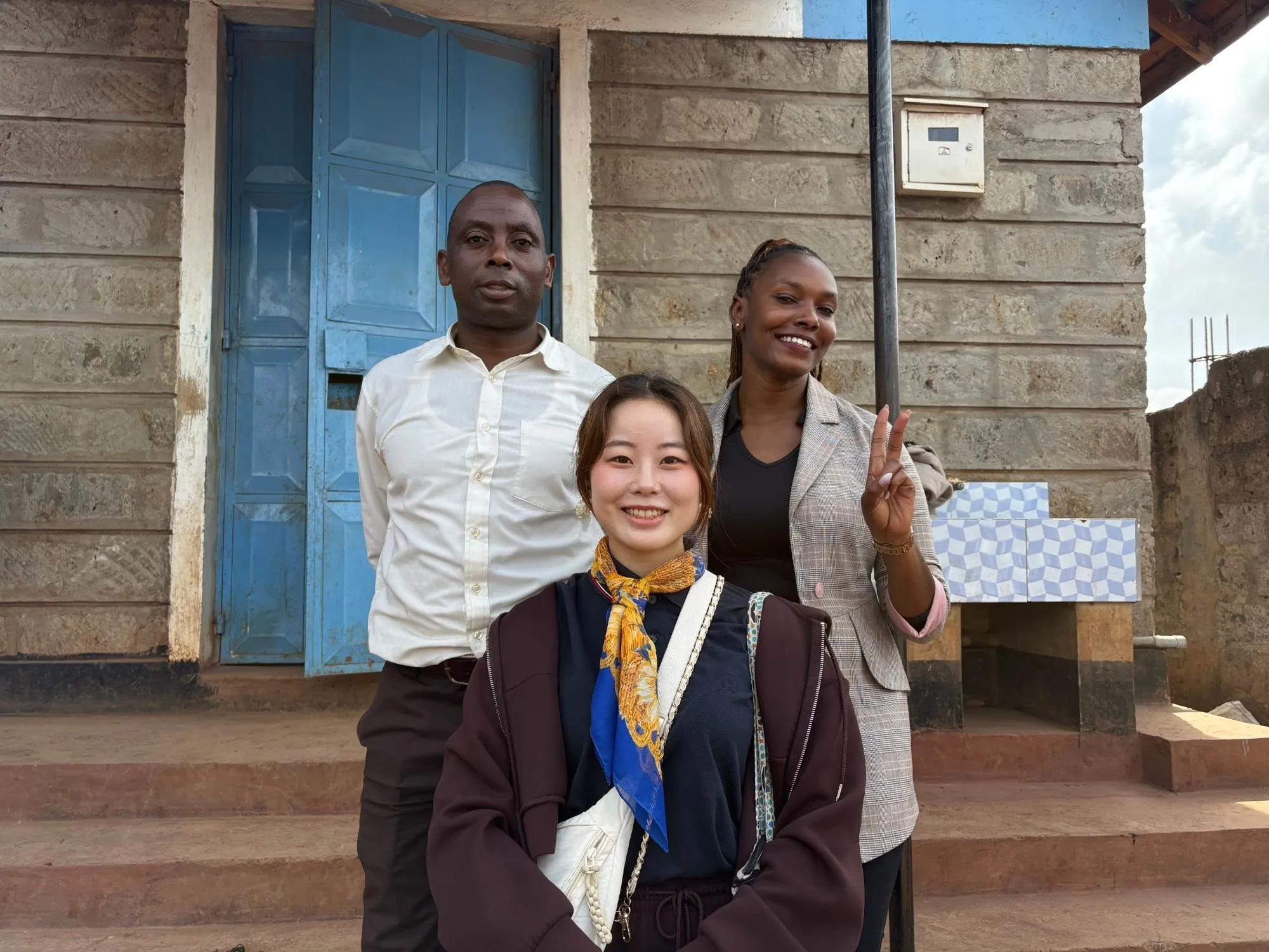 A programme participant with two people in front of a building with a blue door.
