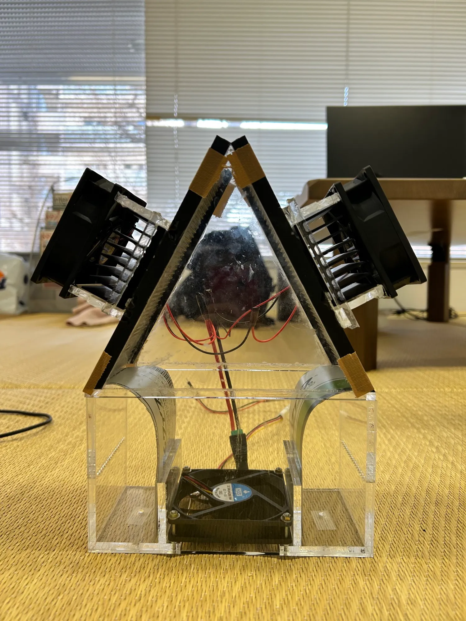 P4: a clear acrylic housing with two fans and heatsinks mounted at an angle, on a wooden table.